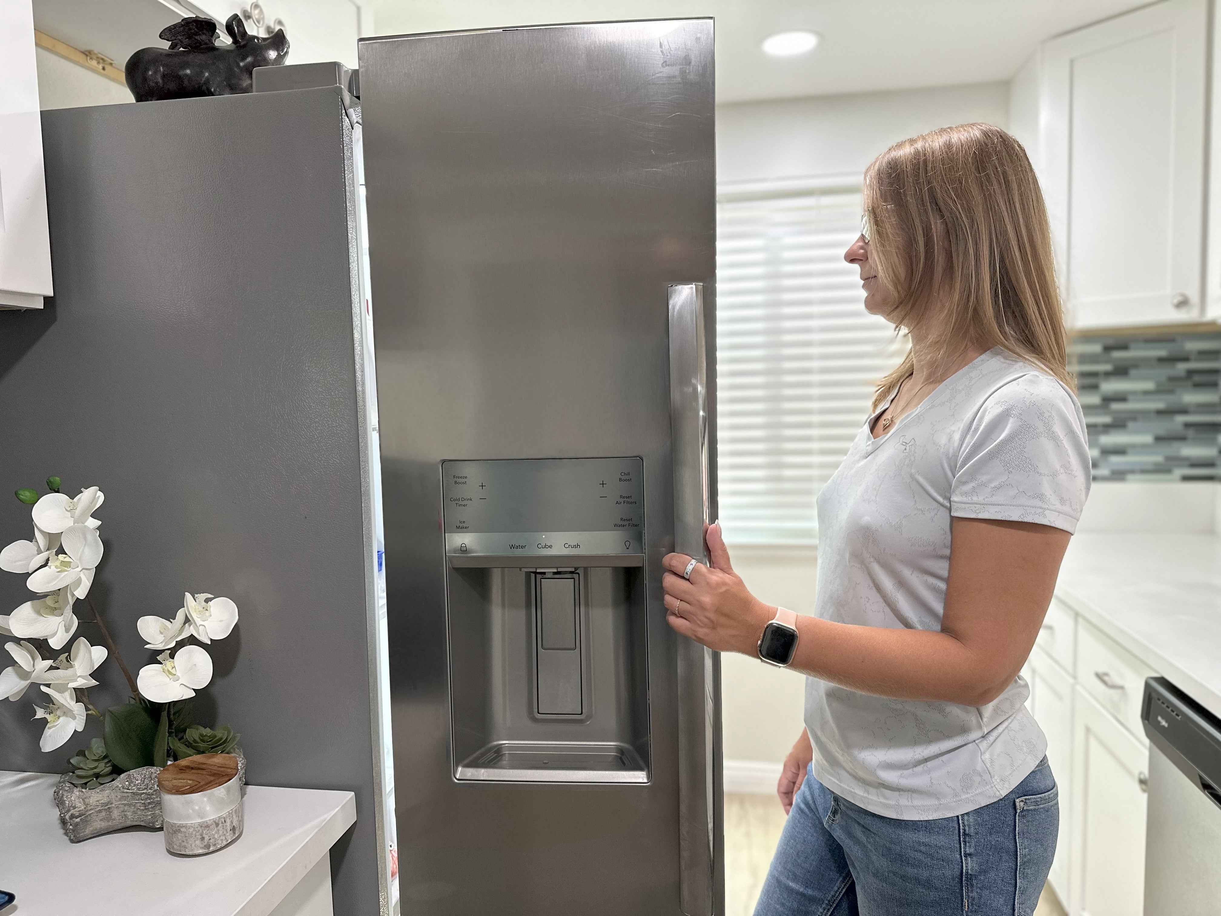 Woman opening a stainless steel refrigerator in a kitchen. No magnets on the fridge door.