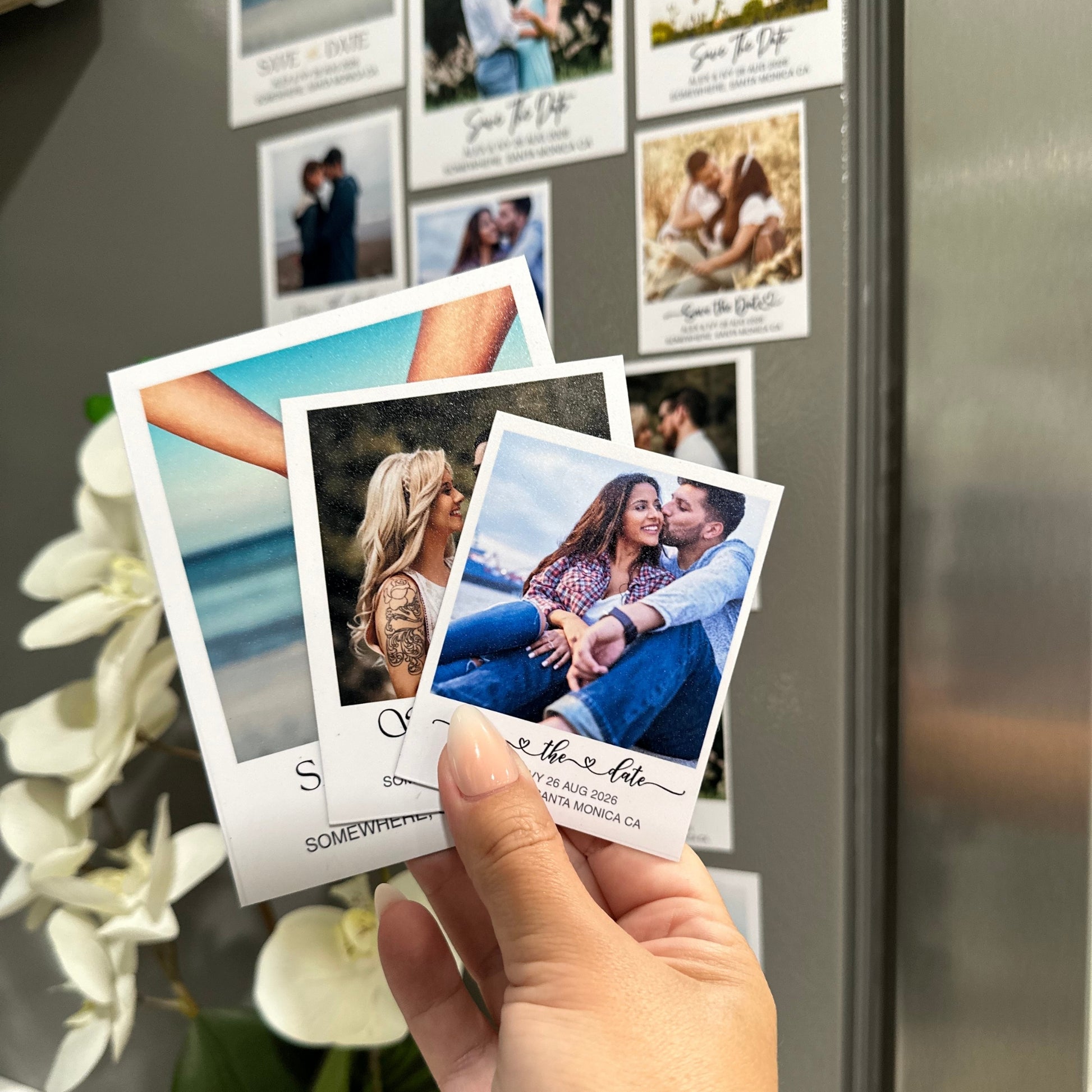Hand holding a set of Save the Date custom photo magnets of 3 sizes against a refrigerator with more photos magnets attached.