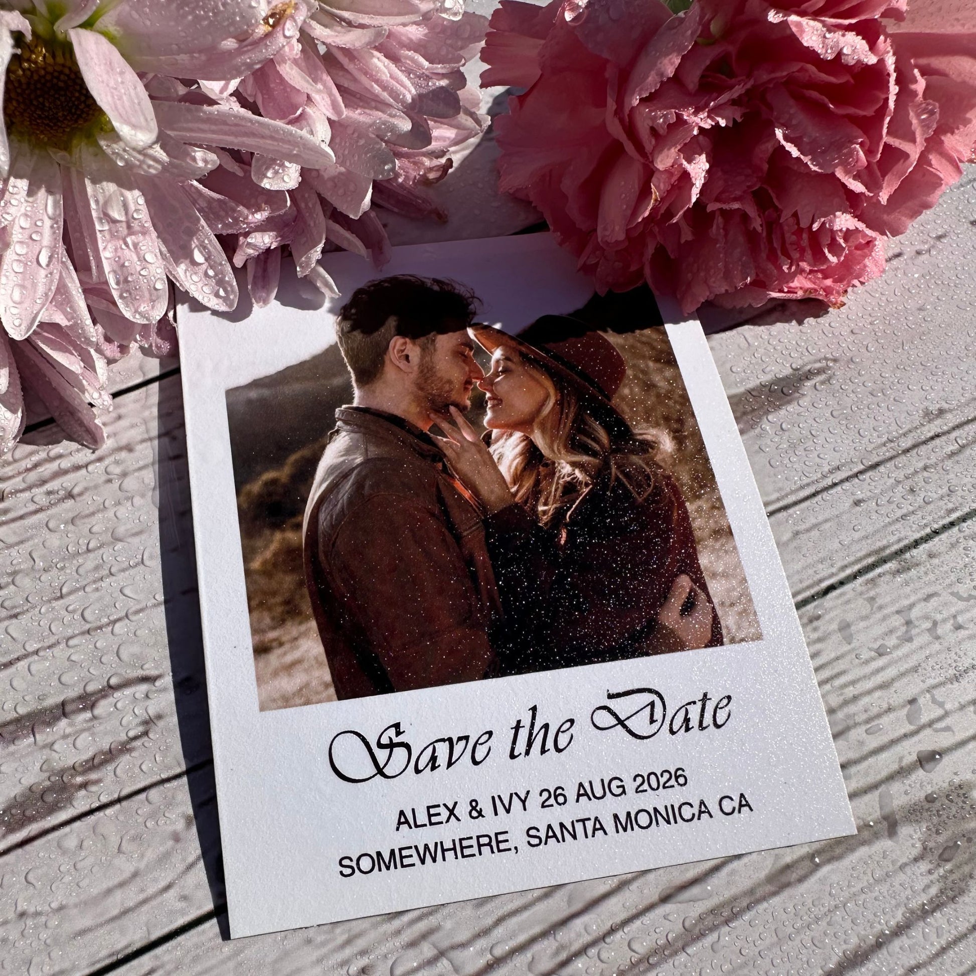 Custom Save the Date Photo Magnets of a couple and pink flowers on a wooden surface with drops of water