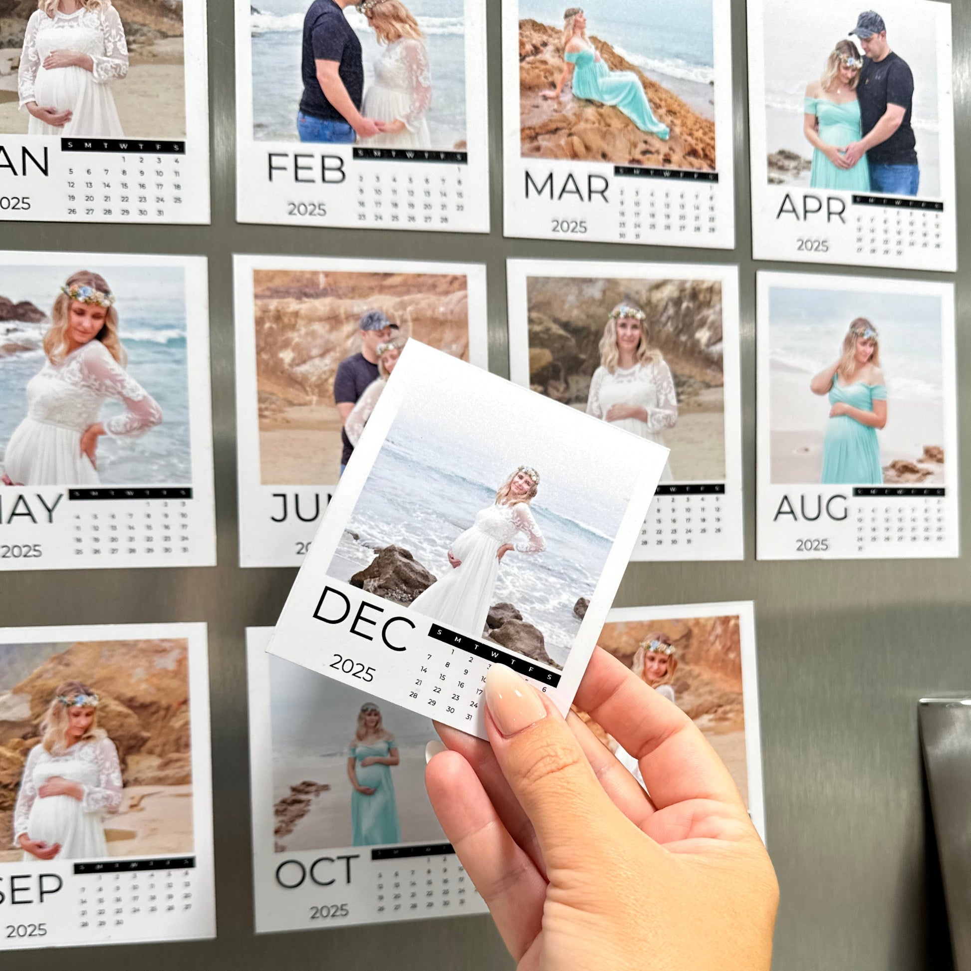 Calendar with various photos of a couple and a pregnant woman, held by a hand in front of a stainless steel refrigerator.