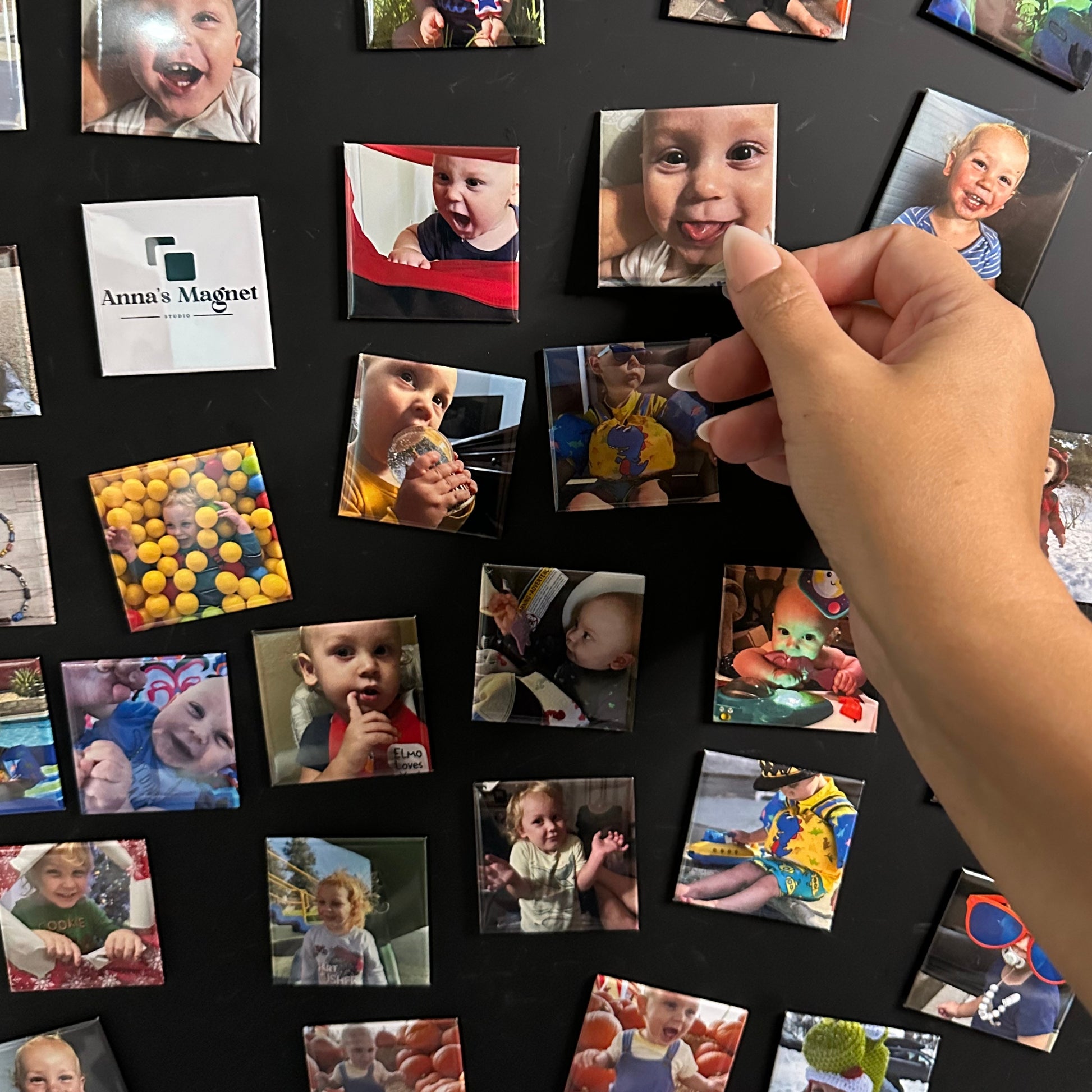 Hand arranging 2x2 custom photo magnets of a baby on a black magnetic chalkboard.