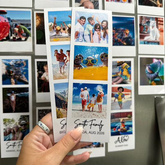 Hand holding a custom photo booth strip magnets with family photos from vacation trips against a stainless steel refrigerator with other custom photo magnets.