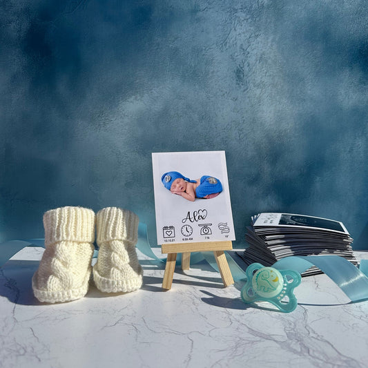 White knitted baby booties, a pacifier, and a custom photo magnet of a new baby on a stand against a blue textured background.