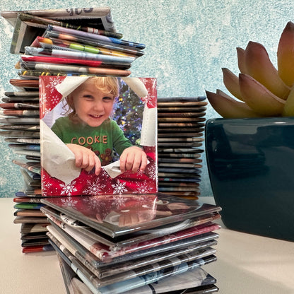Stack of 2x2 custom photo magnets with a magnet with a child and Christmas wrapping paper in front against a textured blue wall.